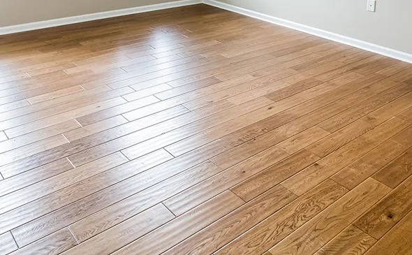 Natural light shining on newly installed hardwood flooring in an empty room with white baseboards and clean finishes.