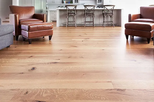 Modern hardwood flooring with a natural wood finish, featuring plush armchairs and a dining area in the background, illustrating quality hardwood floor installation in Willoughby, OH.
